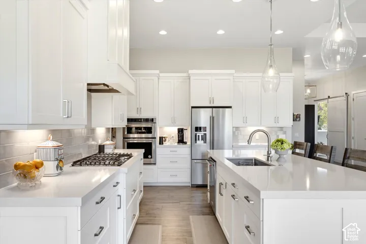 White shaker cabinetry, stainless steel appliances, light-toned countertops, subway tile backsplash, and wood-finish flooring