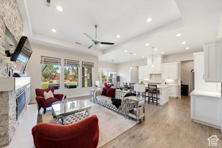 Open concept living space featuring wood-finish flooring, a stone-clad fireplace, and a tray ceiling with recessed lighting