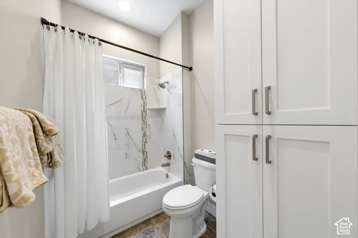 White paneled cabinetry with modern hardware, tiled tub/shower combination with niche, window, recessed lighting, and wood-finish flooring