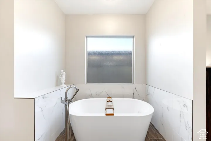 Freestanding soaking tub with floor-mounted faucet, marble-finish tile surround, and an opaque privacy window