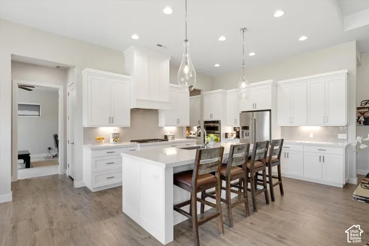 Contemporary kitchen featuring white cabinetry, a large center island with seating, stainless steel appliances, and wood-finish flooring