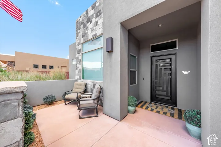 Modern exterior featuring stacked stone accents, a geometric entry door, a covered entry, and a paved patio area