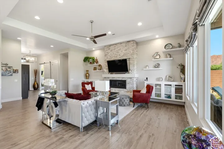 Recessed lighting illuminates wood-finish flooring, a tray ceiling, and a stone-clad fireplace