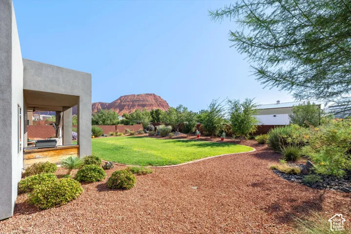 Expansive backyard featuring a manicured lawn, red decorative rock landscaping, mature trees, and a covered patio with an outdoor cooking area