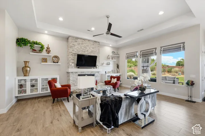 Spacious living area featuring wood-finish flooring, a stone-clad fireplace with a mantel, recessed lighting, and a tray ceiling