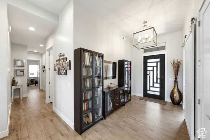 Wood-finish flooring throughout, modern entry door with decorative glass, recessed ceiling lighting, and a contemporary chandelier