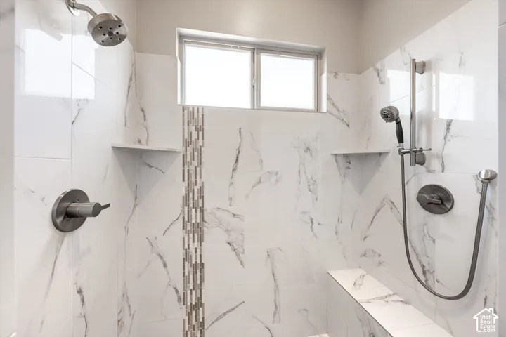 Walk-in shower with marble-look tile, built-in shelving, mosaic tile accent, and transom window