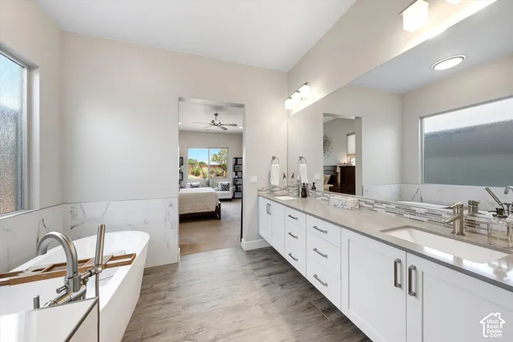 Freestanding soaking tub, dual vanity with quartz countertop, tiled flooring, and a large wall-mounted mirror
