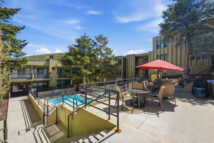Exterior concrete patio with a red umbrella, an outdoor dining set, and a rectangular pool