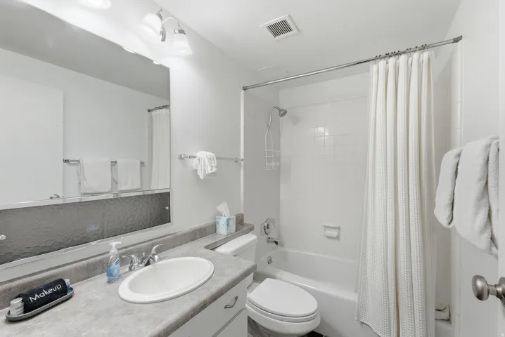 Bathroom featuring a vanity with an integrated sink, a wall-mounted mirror, overhead lighting, a toilet, and a shower-over-tub combination with white subway tile surround
