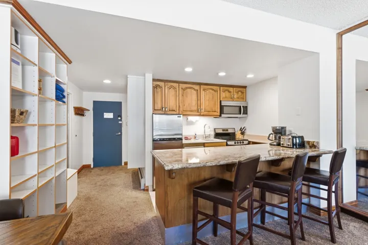 Kitchen featuring an eat-in counter with stone-finish countertop, wood cabinetry, built-in stainless steel microwave, and a stainless steel refrigerator