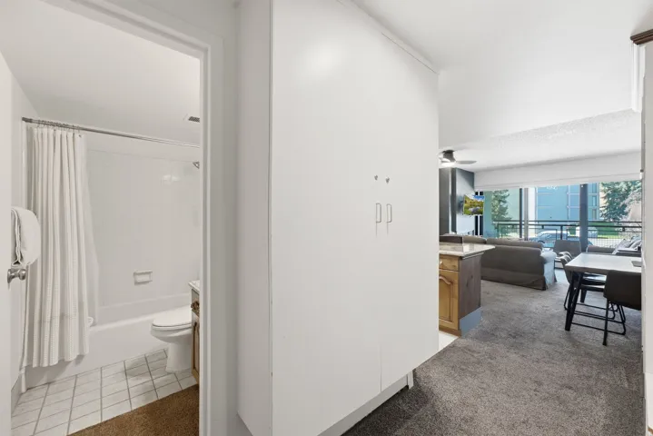 White tiled bathroom with a tub/shower combination, and a separate living area featuring a ceiling fan and carpeted flooring