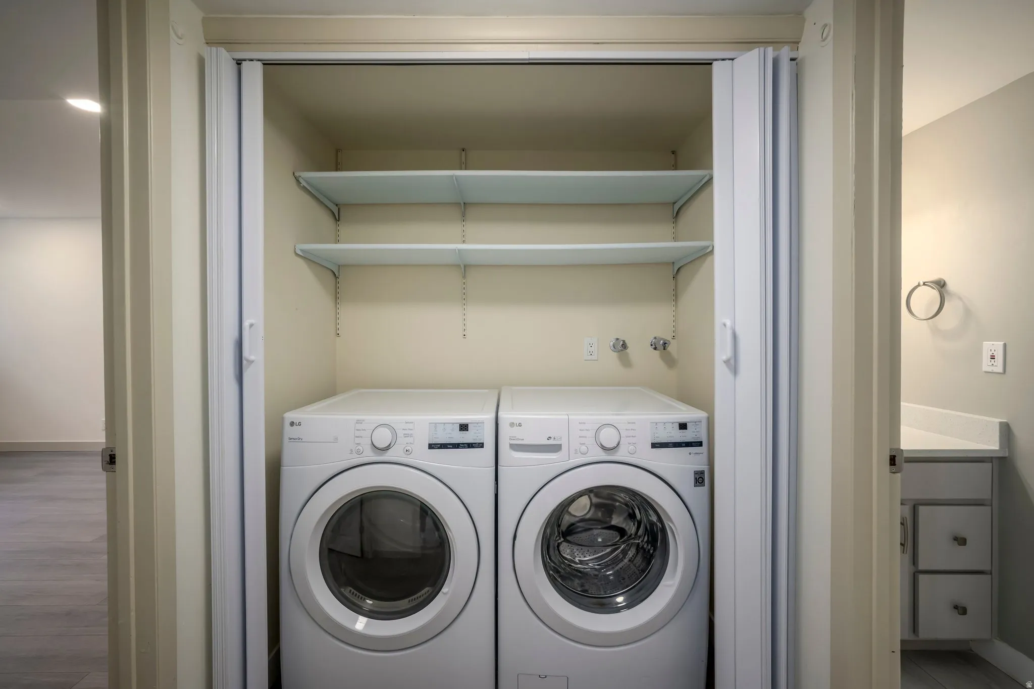 Laundry closet with bi-fold doors, white washer and dryer units, and two wall-mounted shelves