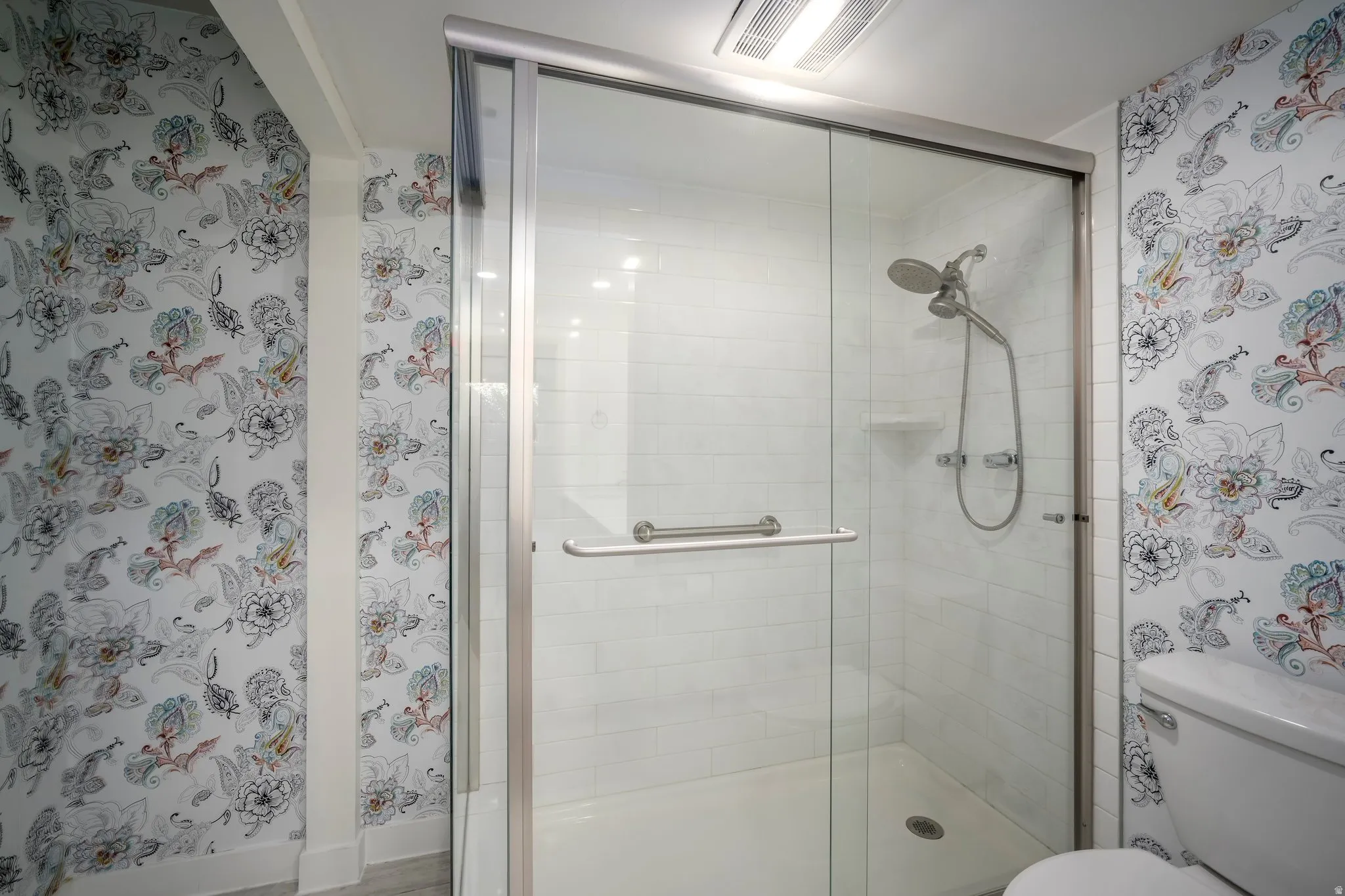 Glass-enclosed shower with subway tile surround, rainfall shower head, and an integrated grab bar