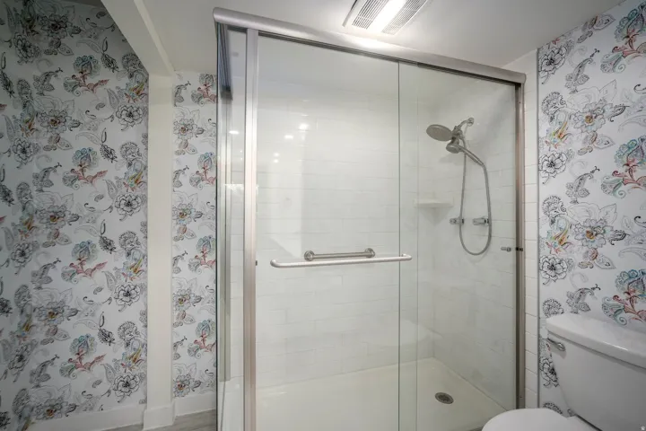 Glass-enclosed shower with subway tile surround, rainfall shower head, and an integrated grab bar
