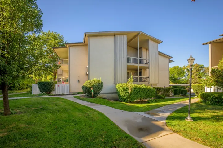 Two-story stucco exterior, multiple private balconies, concrete pathways, mature landscaping, and an outdoor lantern-style light fixture