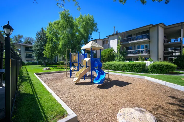 Community playground with wood chip surfacing, bordered by manicured lawn and mature trees