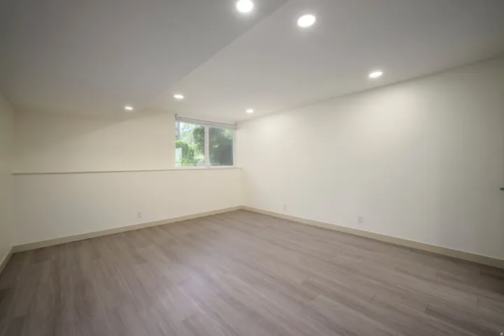 Recessed lighting with a white ceiling, light wood-finish flooring, and a window with a roller shade