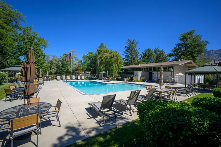 Expansive outdoor pool area with surrounding concrete patio, multiple seating arrangements, mature landscaping, and a mountain backdrop