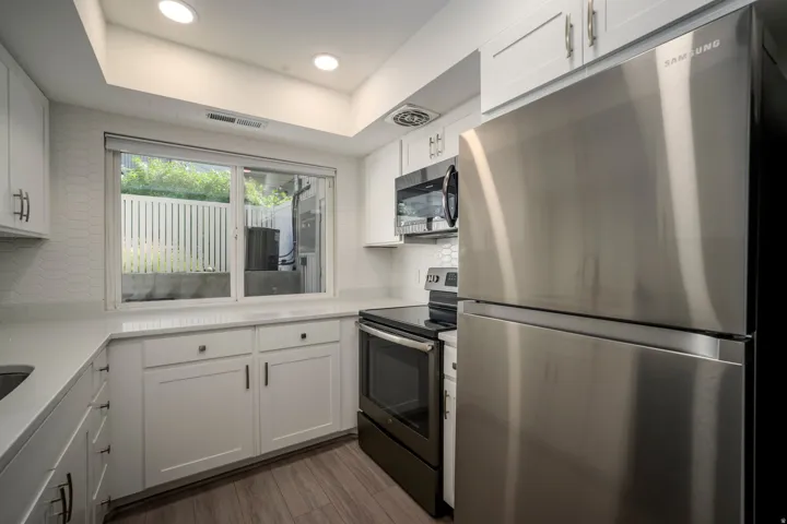White shaker-style cabinetry, stainless steel appliances, light-toned countertops, contemporary geometric tile backsplash, and wood-finish flooring