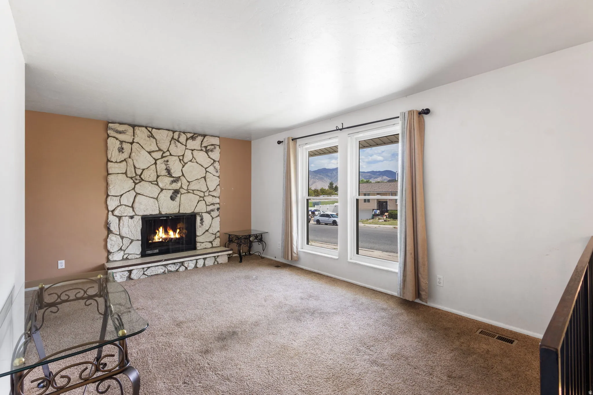 Stone-clad fireplace with hearth, dual pane windows, and carpeting