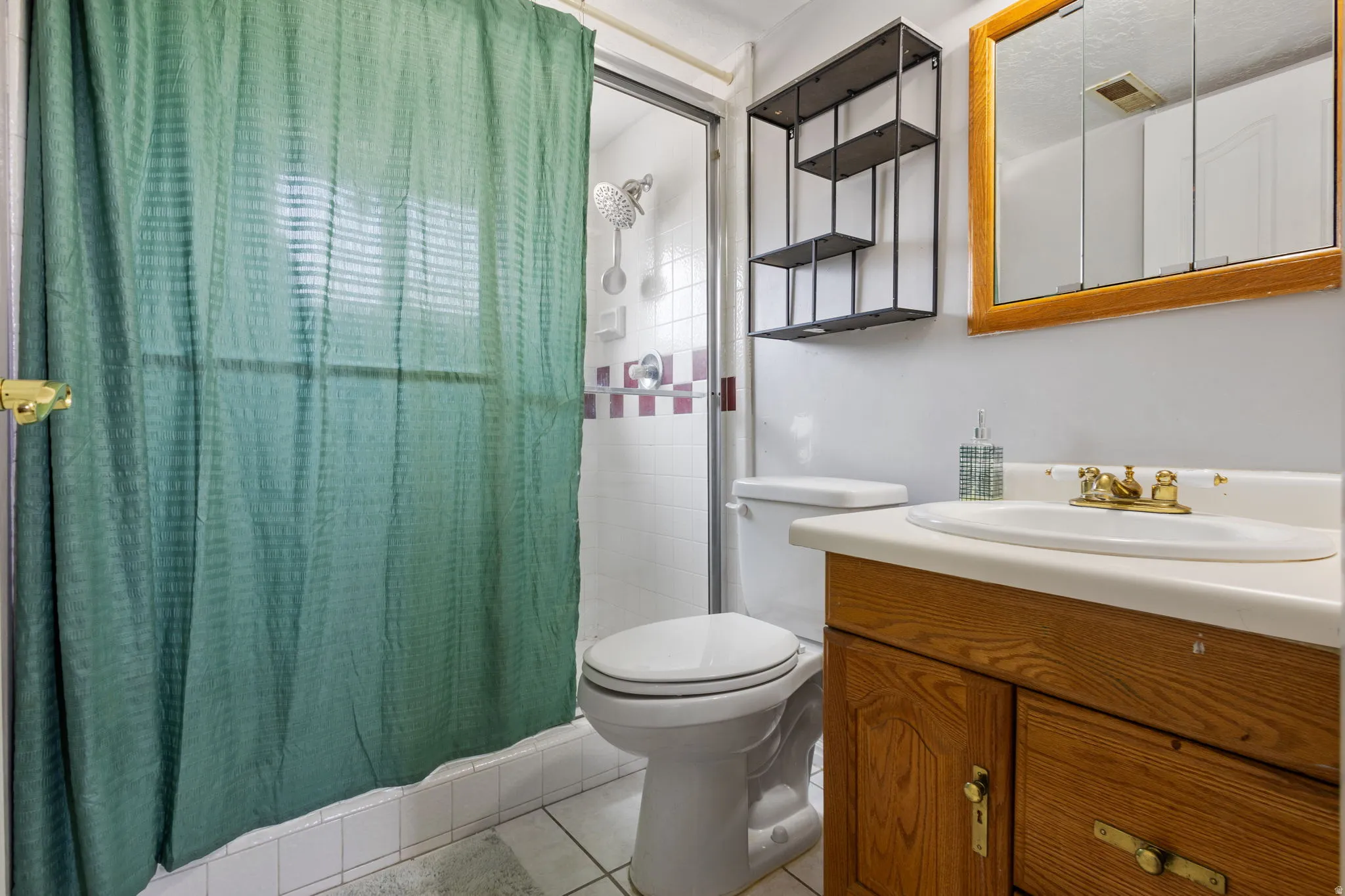 Bathroom featuring a wood-finish vanity with an integrated sink, a framed medicine cabinet, and a tiled shower with decorative accent tiling