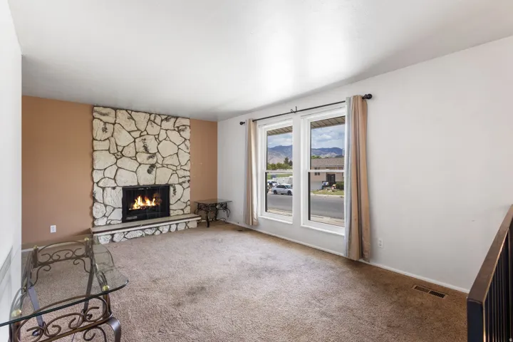 Stone-clad fireplace with hearth, dual pane windows, and carpeting