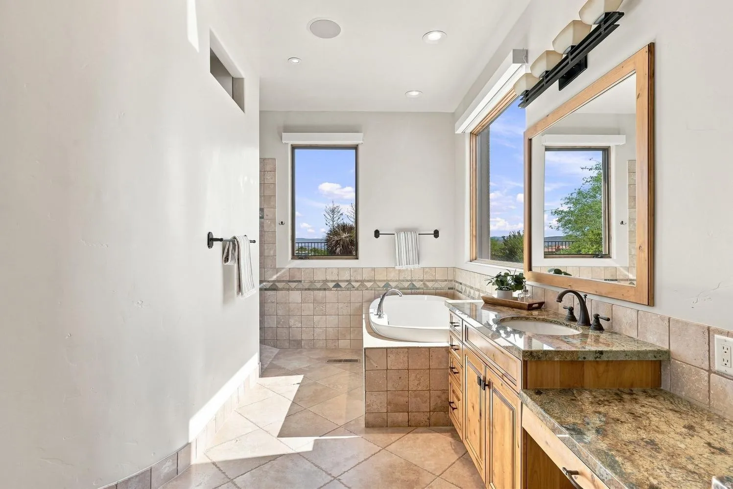Bathroom featuring a built-in soaking tub, dual windows, a wood-finish vanity with an integrated sink, and stone countertops