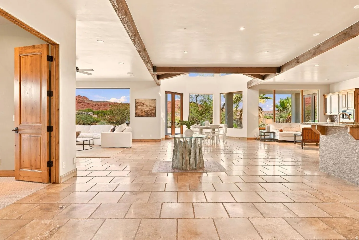 Open-concept living space featuring large format tile flooring, natural wood ceiling beams, and expansive windows