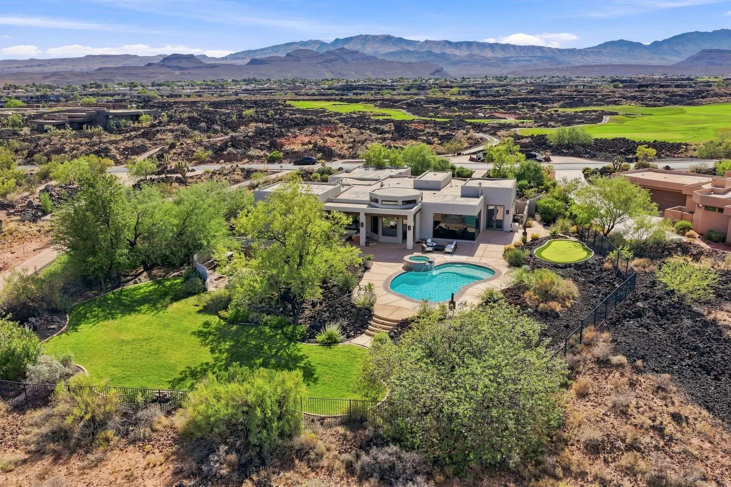 Contemporary architecture with a flat roofline, an irregular-shaped swimming pool, an integrated spa, a private putting green, and mature landscaping
