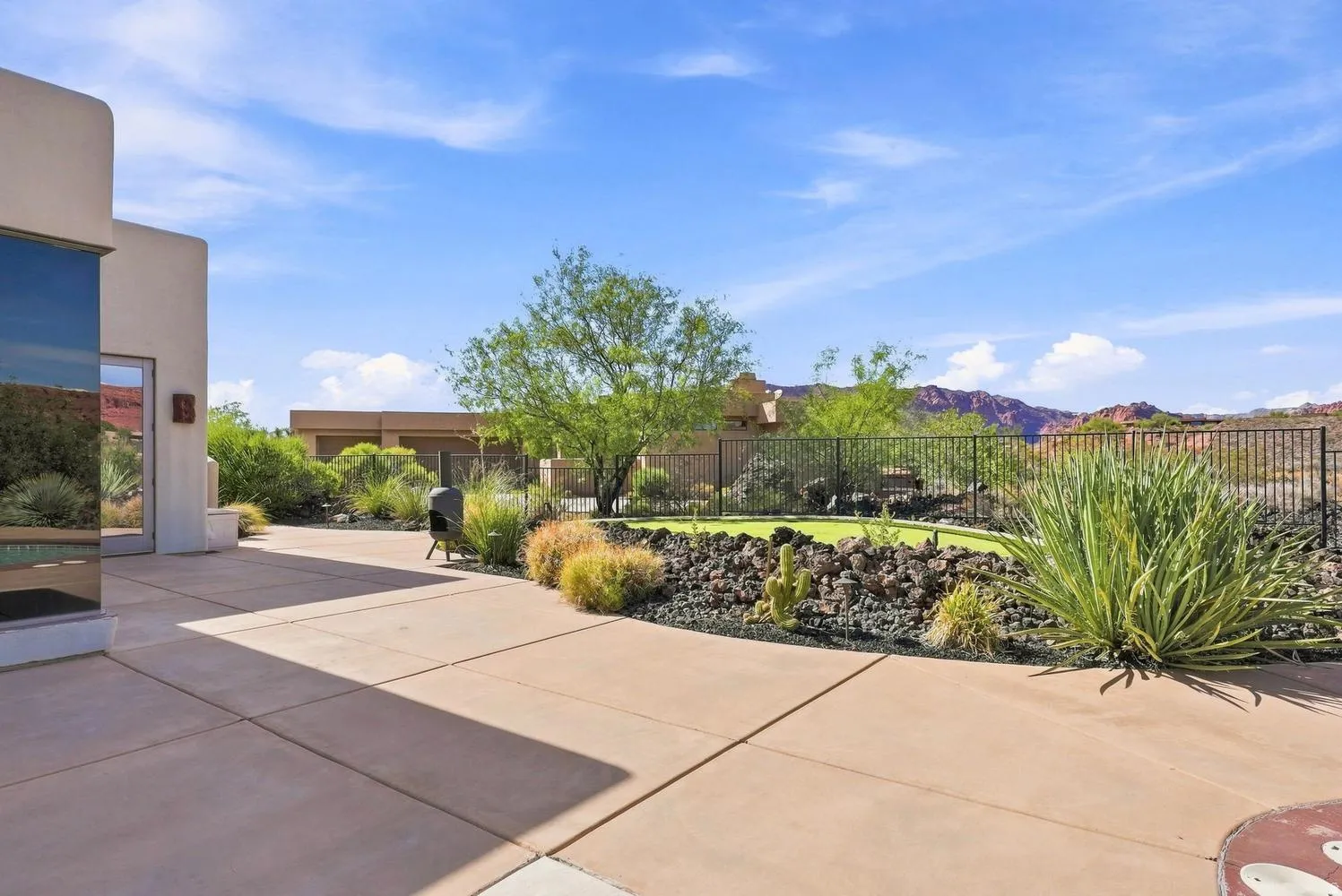 Expansive concrete patio with a desert-adapted landscape, putting green, and a black wrought-iron fence