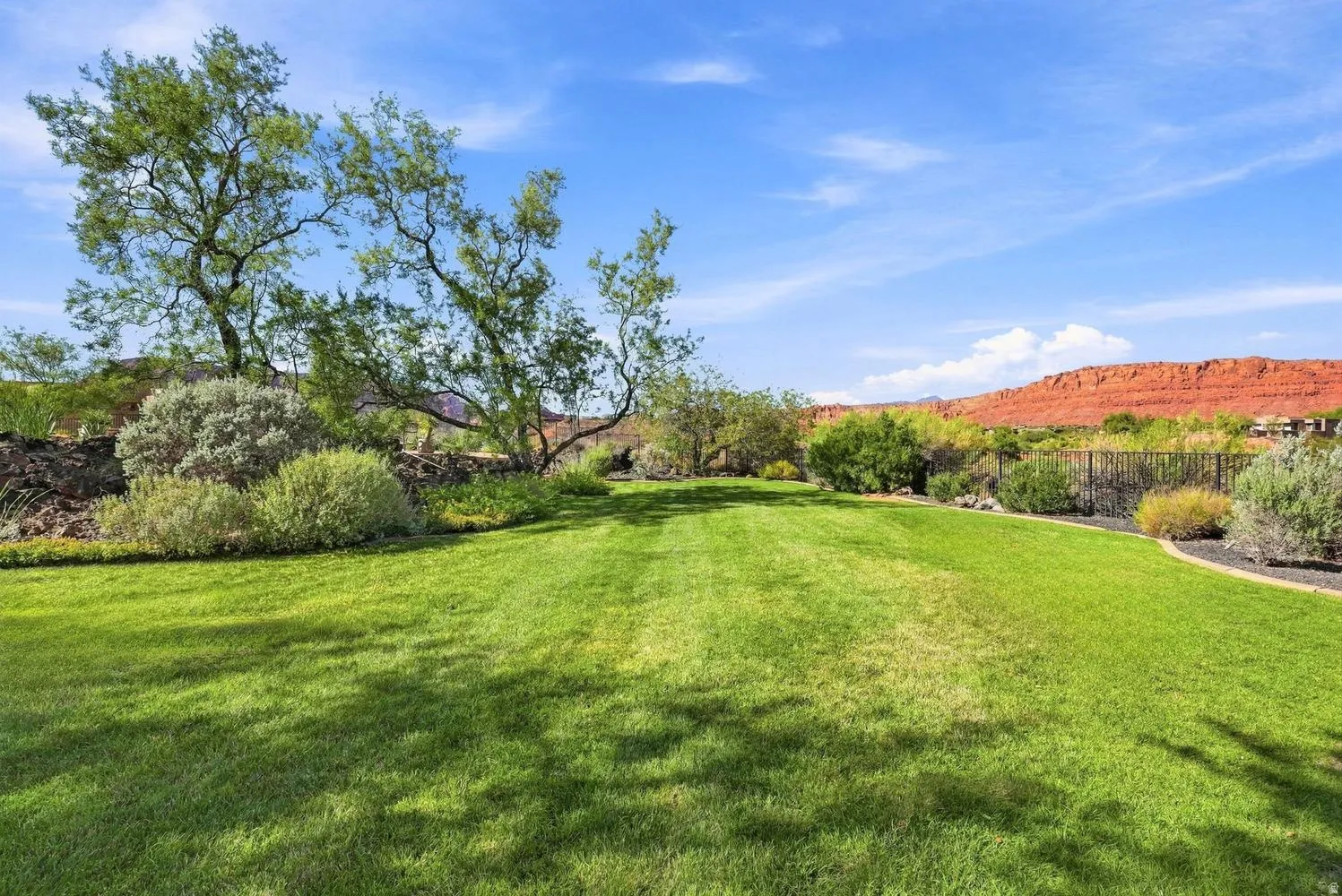 Expansive lawn area, mature trees, landscaped perimeter, and a dark metal fence