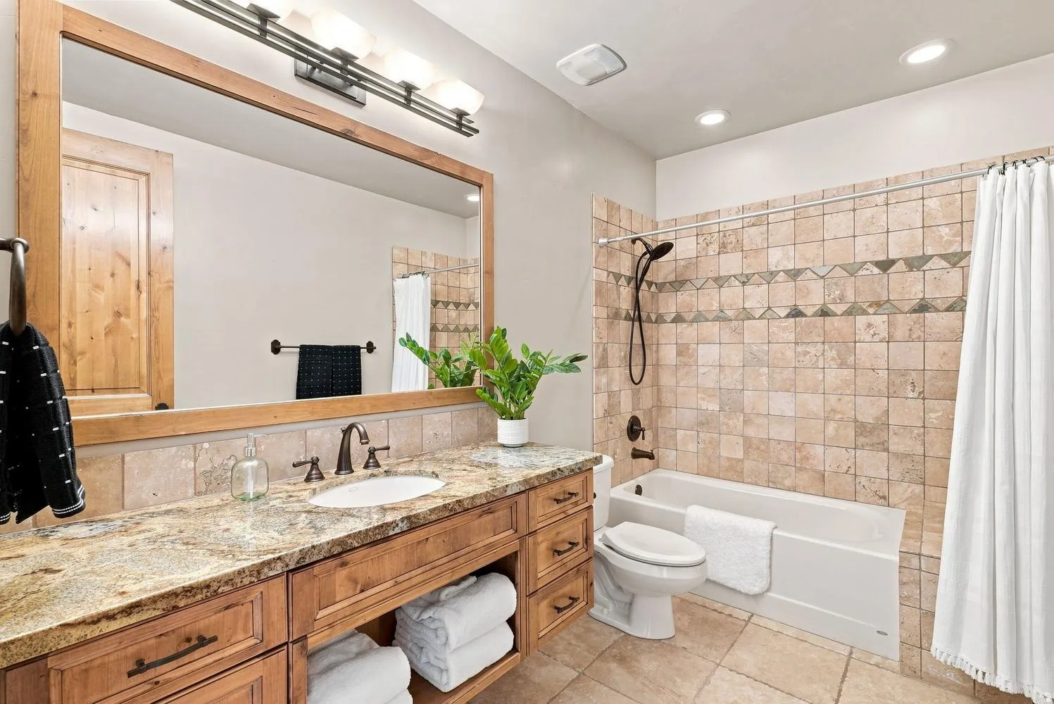 Wood-finish vanity with an undermount sink, stone countertop, and a large framed mirror