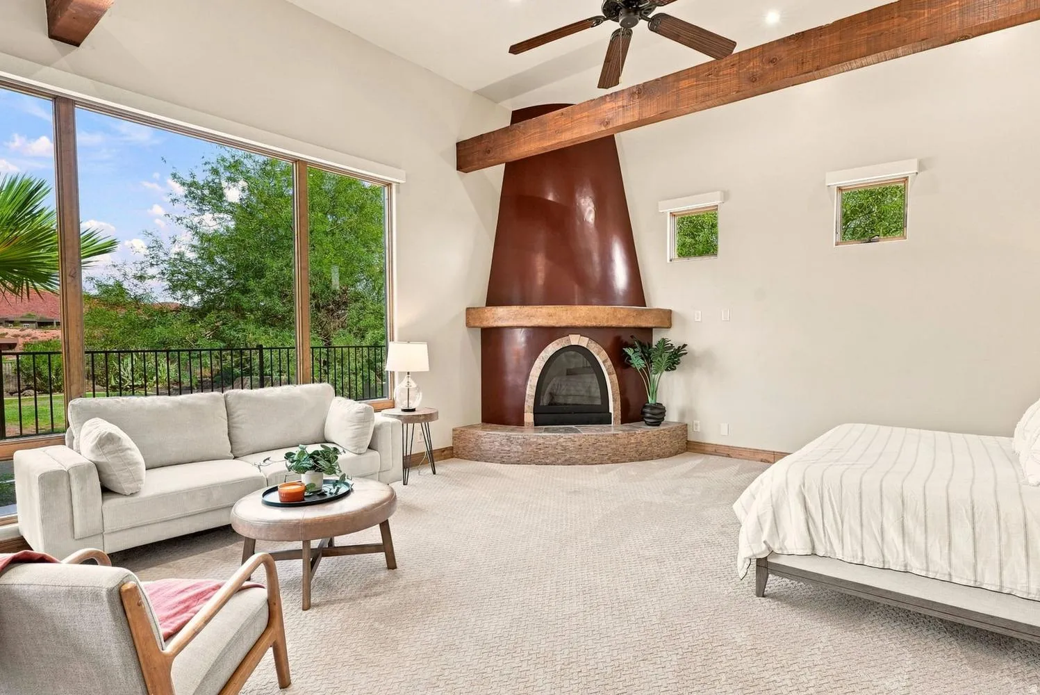 Vaulted ceiling with exposed wood beams, large format windows with outdoor access, built-in fireplace with a stone hearth, ceiling fan, and carpeted flooring