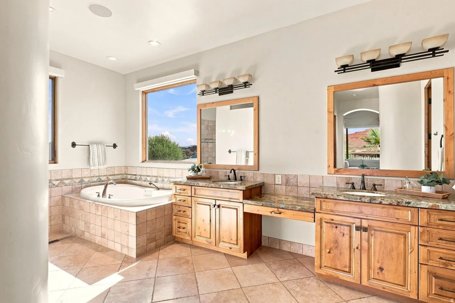 Built-in jetted tub, dual wood vanities with granite countertops, tiled flooring, and multiple windows