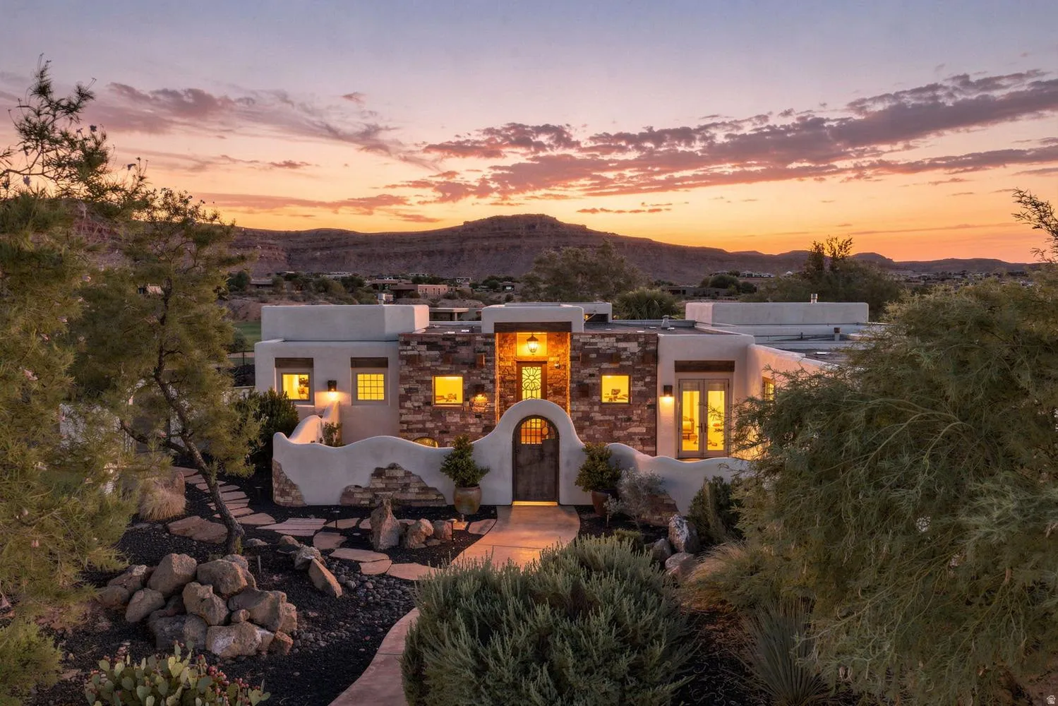 Southwestern architecture with stone accents, a stucco exterior, an arched entry door, and desert landscaping