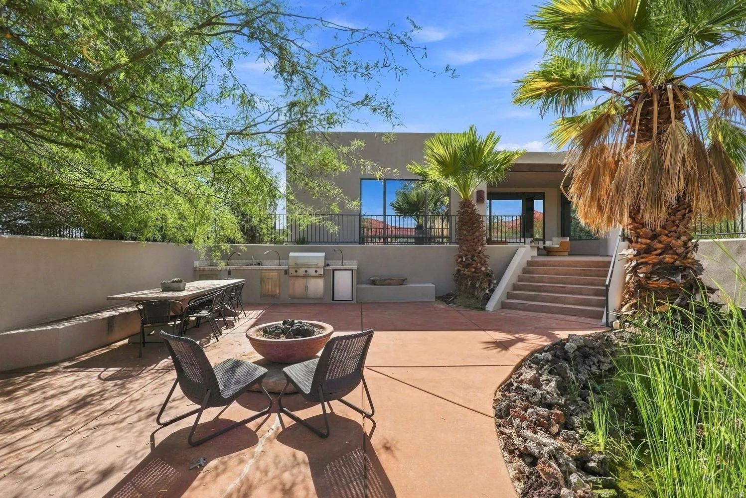 Expansive patio featuring a built-in outdoor kitchen, integrated fire pit, and mature palm trees