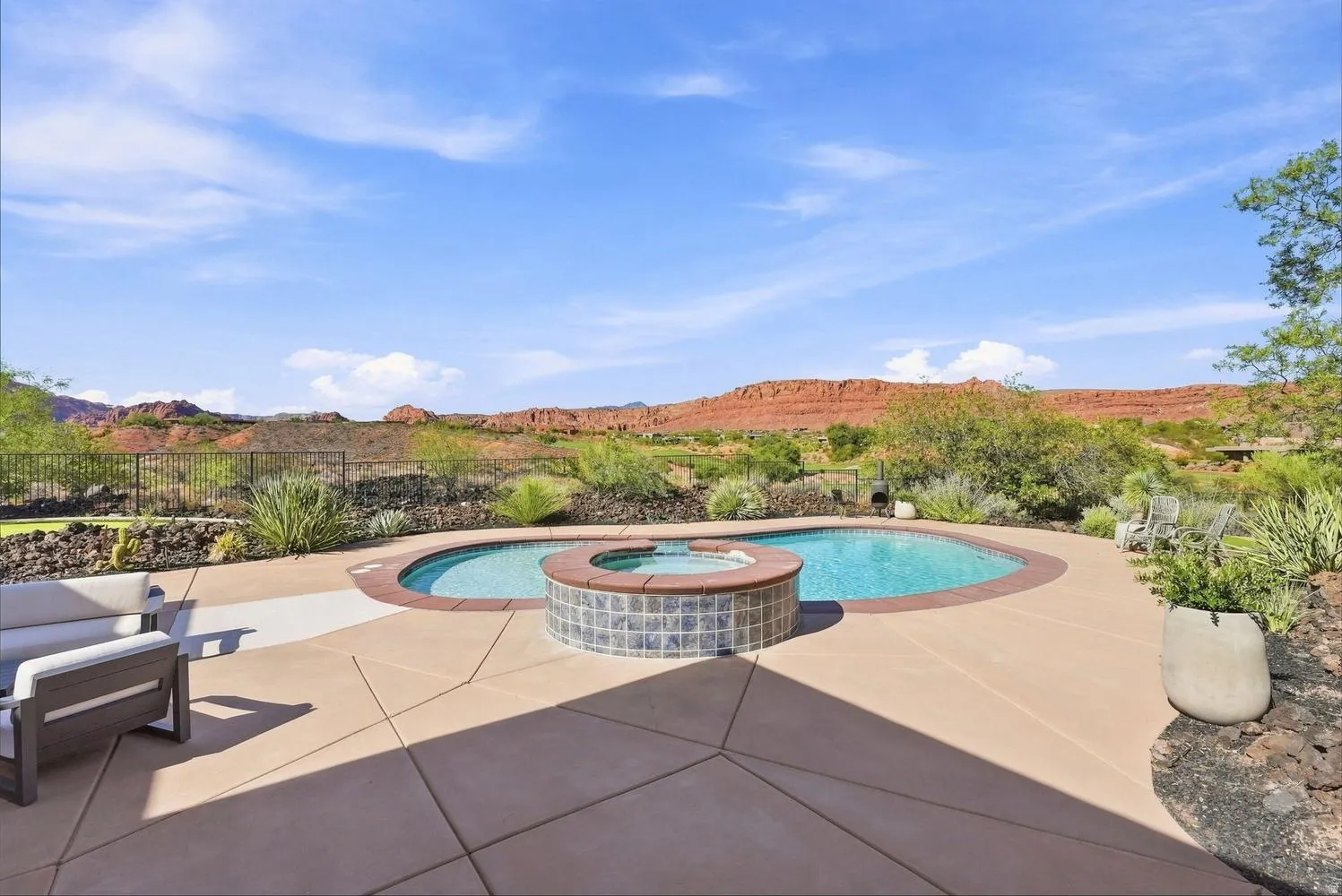 Curved swimming pool with integrated spa, concrete patio, and a desert landscape backdrop with distant red rock formations