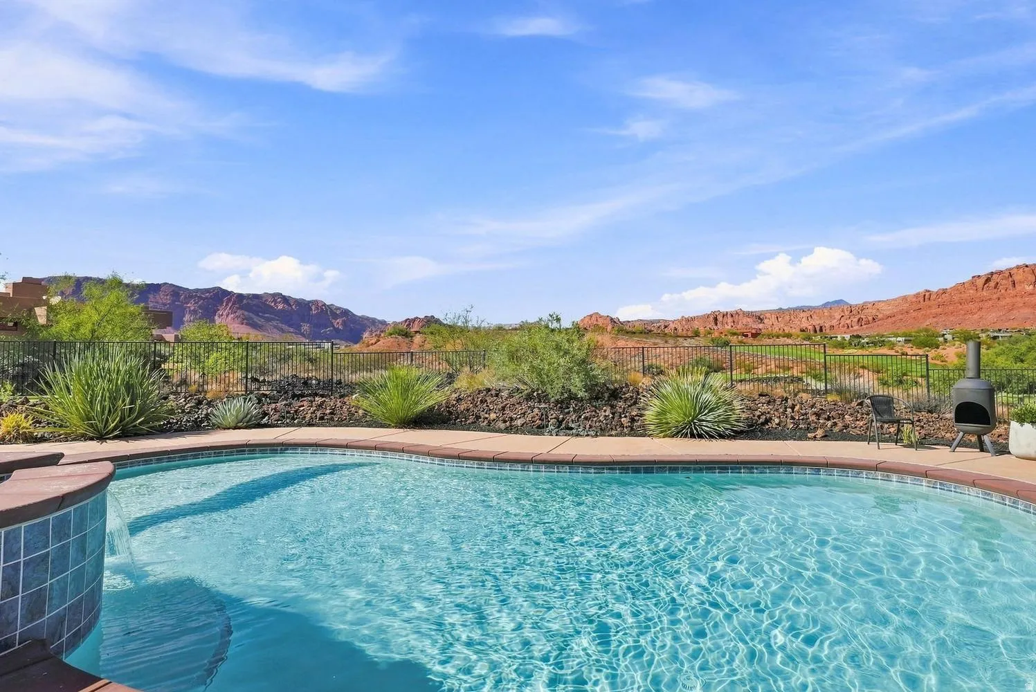 Curved swimming pool with tiled spa, surrounding concrete decking, and desert landscaping