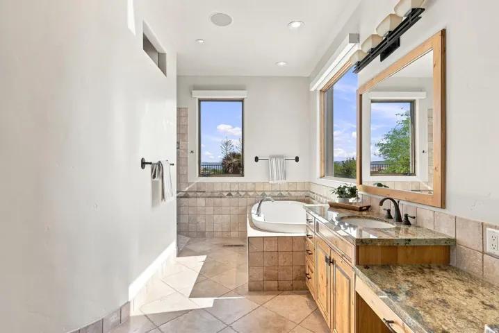 Bathroom featuring a built-in soaking tub, dual windows, a wood-finish vanity with an integrated sink, and stone countertops