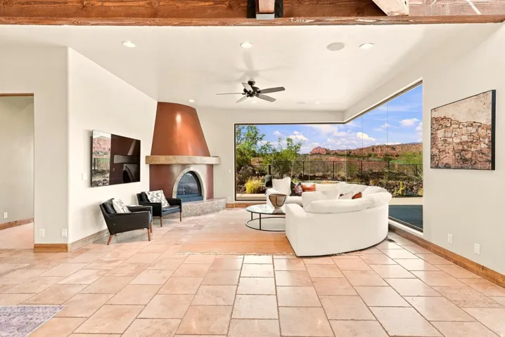 Exposed wood beams, tiled flooring, built-in fireplace with a copper hood, modern ceiling fan, and expansive floor-to-ceiling windows