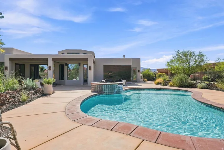 Freeform swimming pool with tiled spa, expansive concrete decking, and xeriscape landscaping