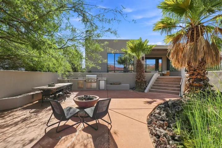 Expansive patio featuring a built-in outdoor kitchen, integrated fire pit, and mature palm trees