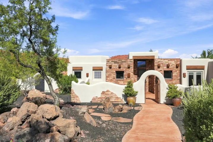 Southwestern-style exterior featuring a stucco and stone facade, arched entryway, and a winding stone pathway