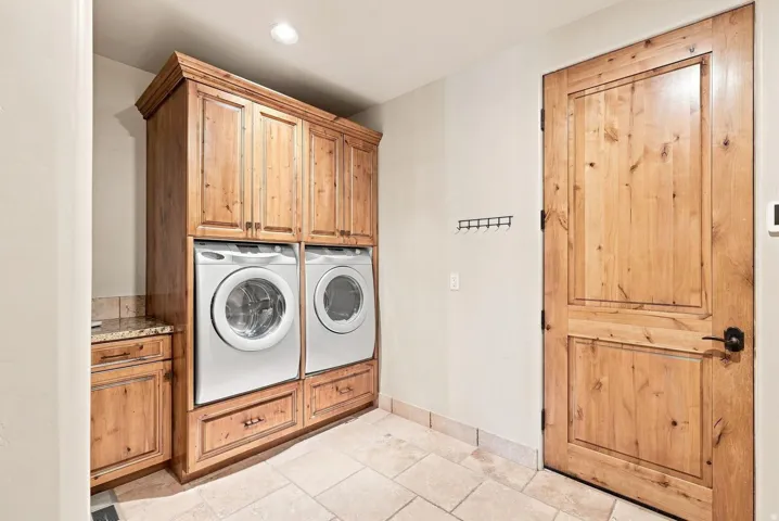 Laundry area with a full-size washer and dryer, custom wood cabinetry, granite-finish countertop with backsplash, and tiled flooring