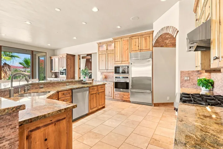 Spacious kitchen featuring natural wood cabinetry, stainless steel appliances, granite countertops, and tile flooring