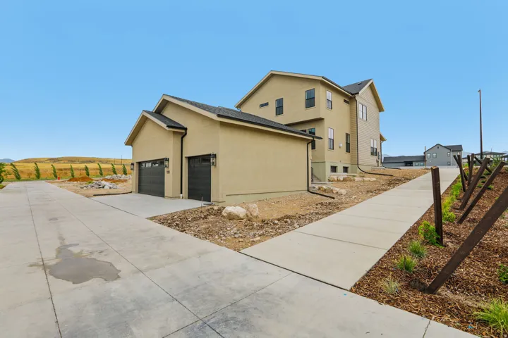 Tan stucco exterior with dark trim windows, dark garage doors, concrete driveway, and a paved walkway
