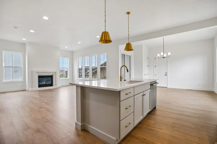 Open-concept living space featuring wood-finish flooring, a kitchen island with stone countertop, stainless steel appliances, a fireplace with a mantel, and multiple windows