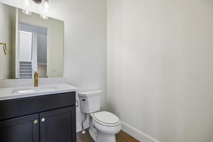 Vanity with a white countertop and integrated sink, gold-finish faucet, dark cabinetry with gold-tone hardware, and wood-finish flooring