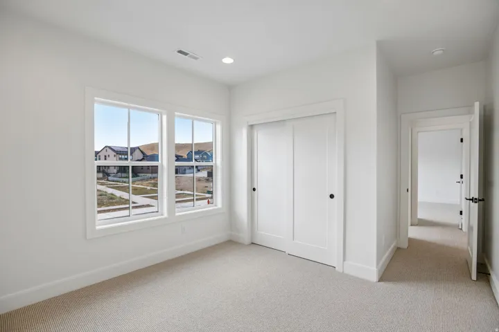 Carpeted room featuring dual windows with white trim, a recessed ceiling light, and a double sliding closet door with matte black hardware